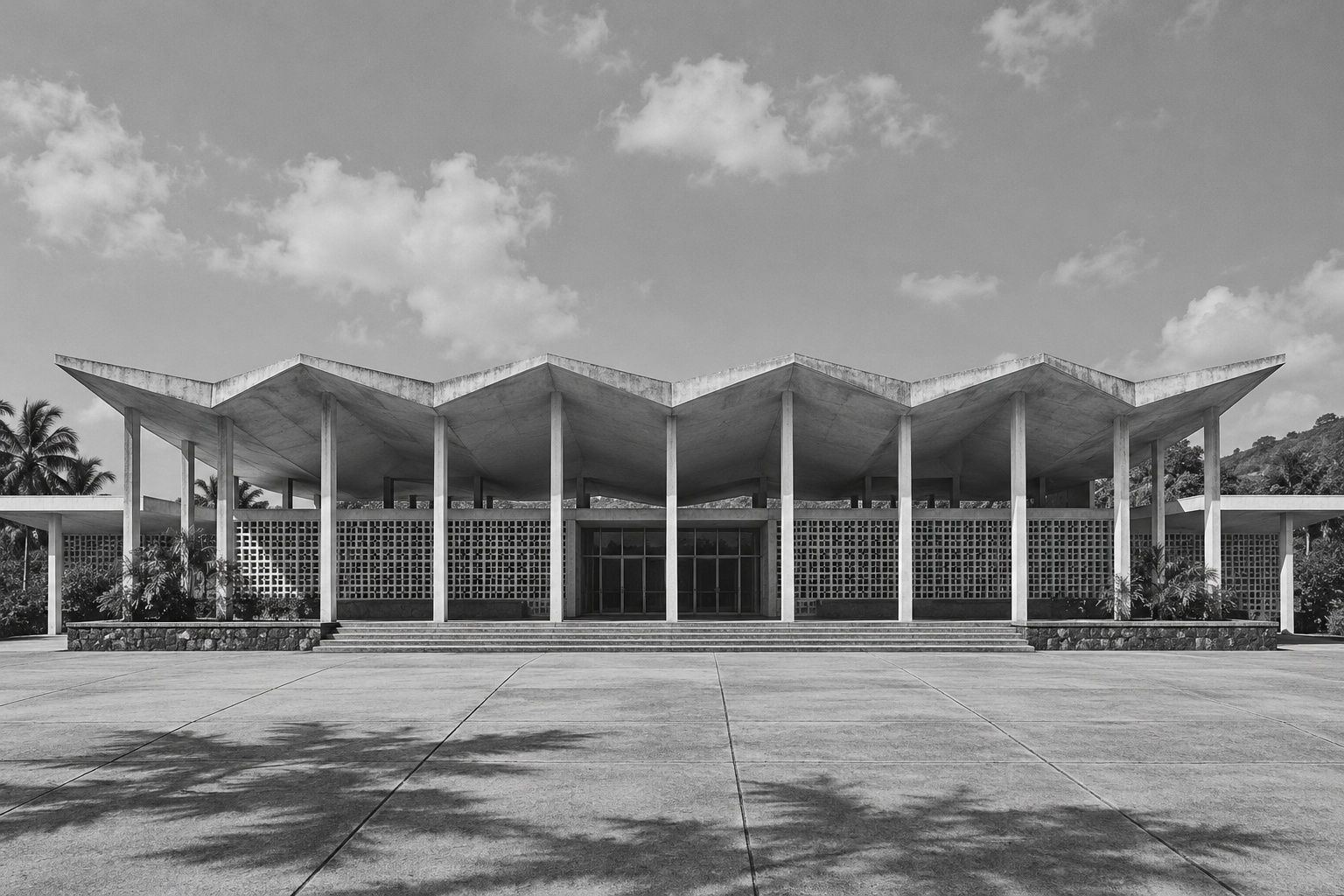 Black and white view of a long modernist civic hall with a folded concrete roof and slim columns