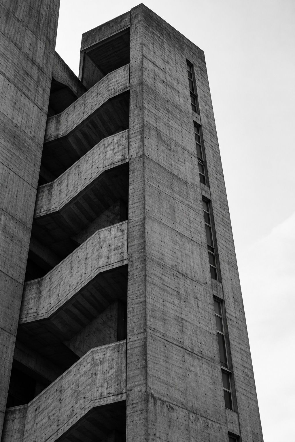 Black and white view up a brutalist concrete stair tower with a vertical slot of windows